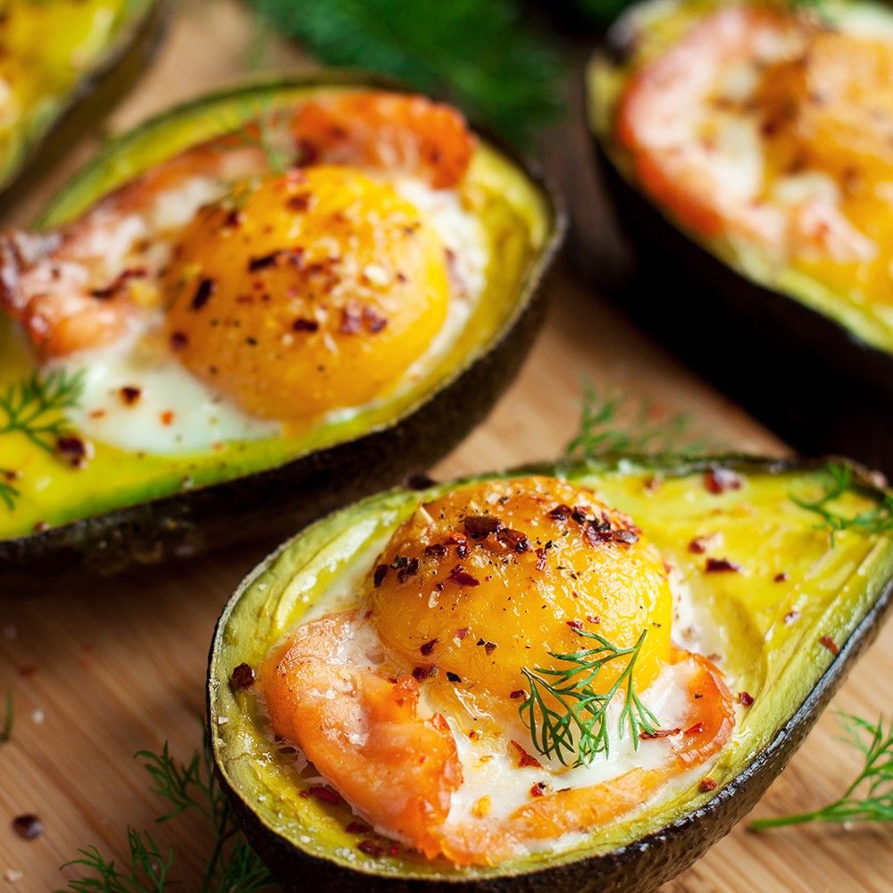 Avocados mit Eiern gebacken. Mit Dill und Gewürzen bestreut. Auf einem Holzbrett serviert.
