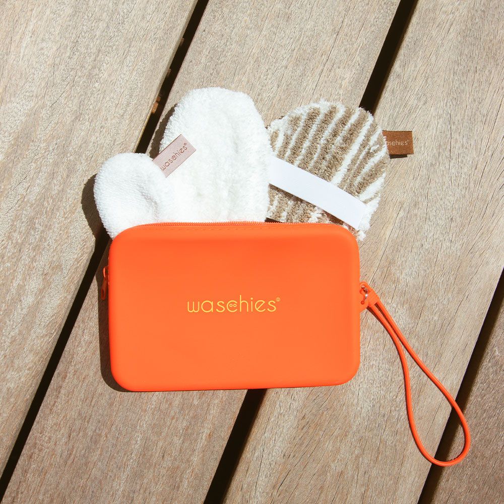 Orangefarbene Tasche mit Reißverschluss und Griff, auf Holz. Enthält drei runde Waschpads. Auf der Tasche steht "waschies".