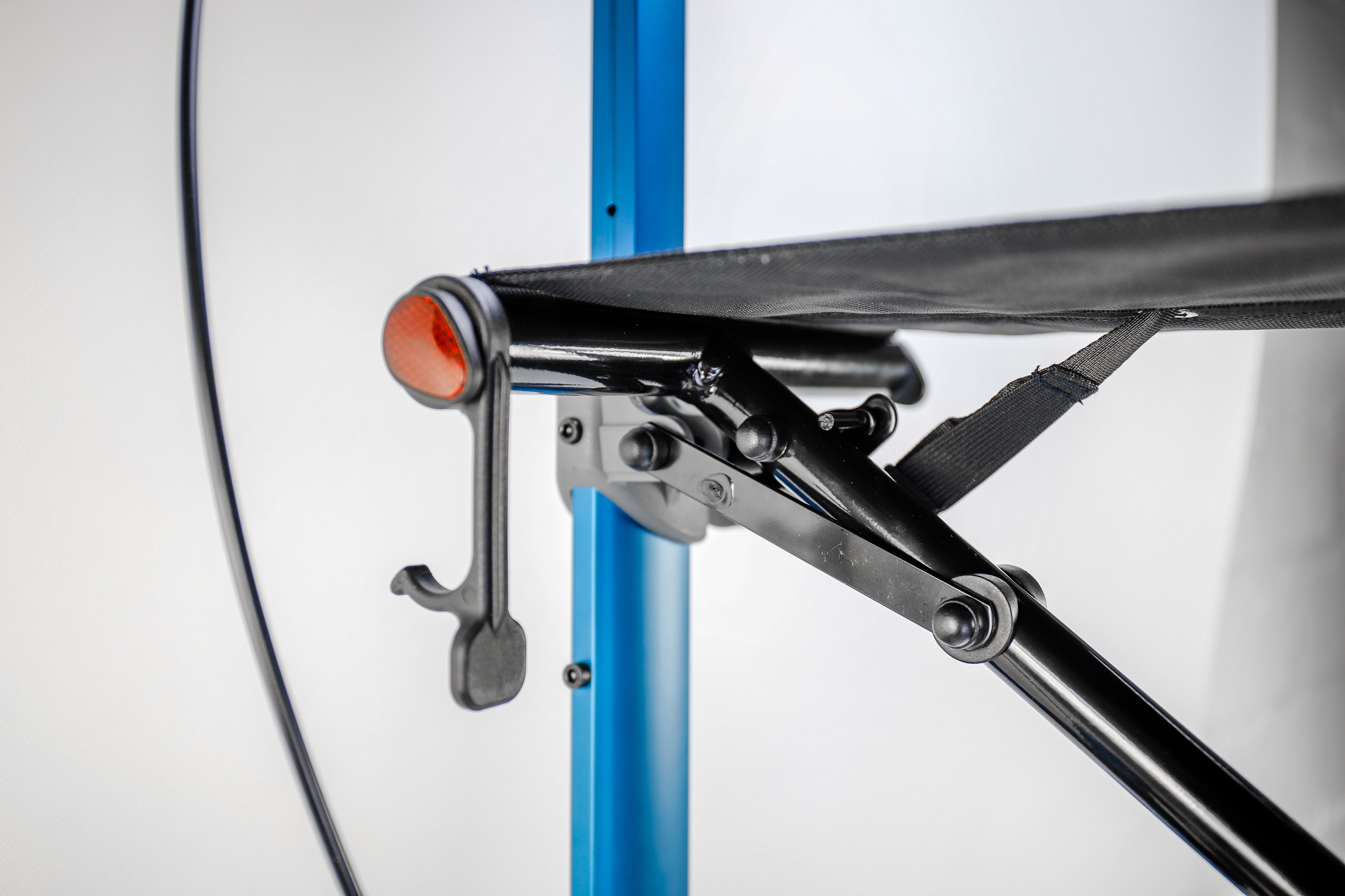 Detailansicht eines Rollators. Schwarze Sitzfläche, blaues Gestell, orangefarbene Akzente. Klappmechanismus sichtbar.