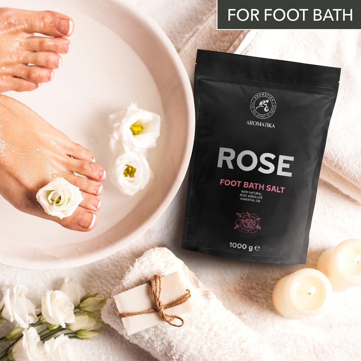 Füße in Wasser mit Rose Fußbadesalz. Schwarzer Beutel mit Aufschrift: Rose. Marke: AROMATIKA. 1000 g. Handtuch, Seife, Kerzen, Blumen.