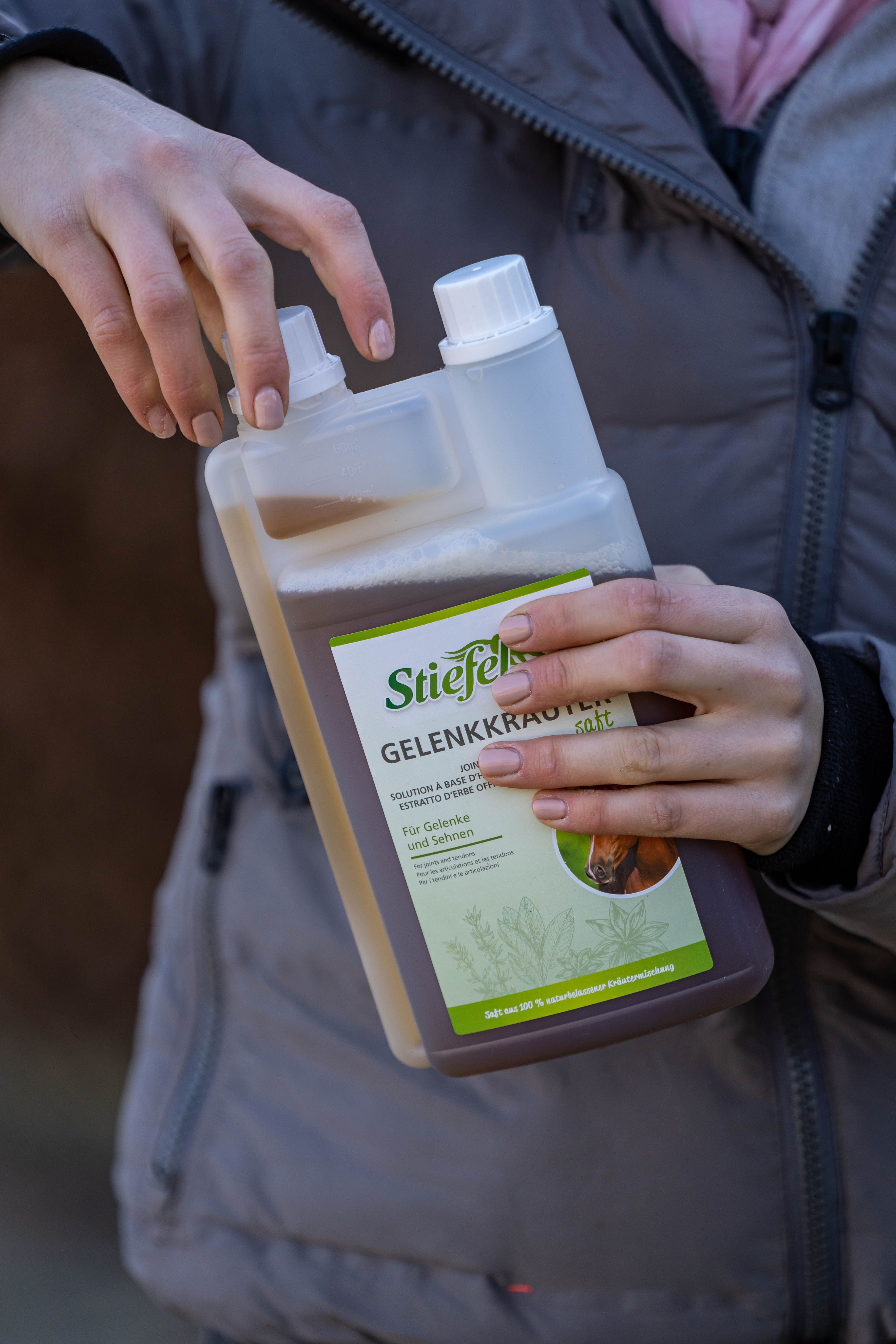 Person hält eine Flasche Stiefel Gelenkkräuter Saft. Die Flasche ist transparent und enthält eine braune Flüssigkeit. Aufschrift: Für Gelenke und Sehnen.
