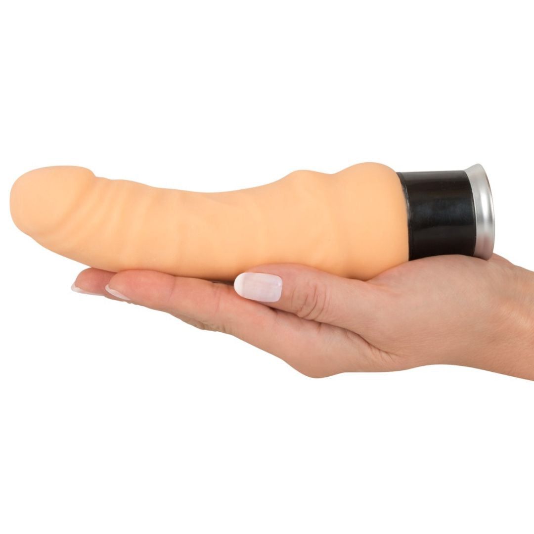 Beigefarbener Vibrator mit geriffelter Oberfläche, gehalten in einer Hand. Schwarzer Sockel mit silbernem Ring.