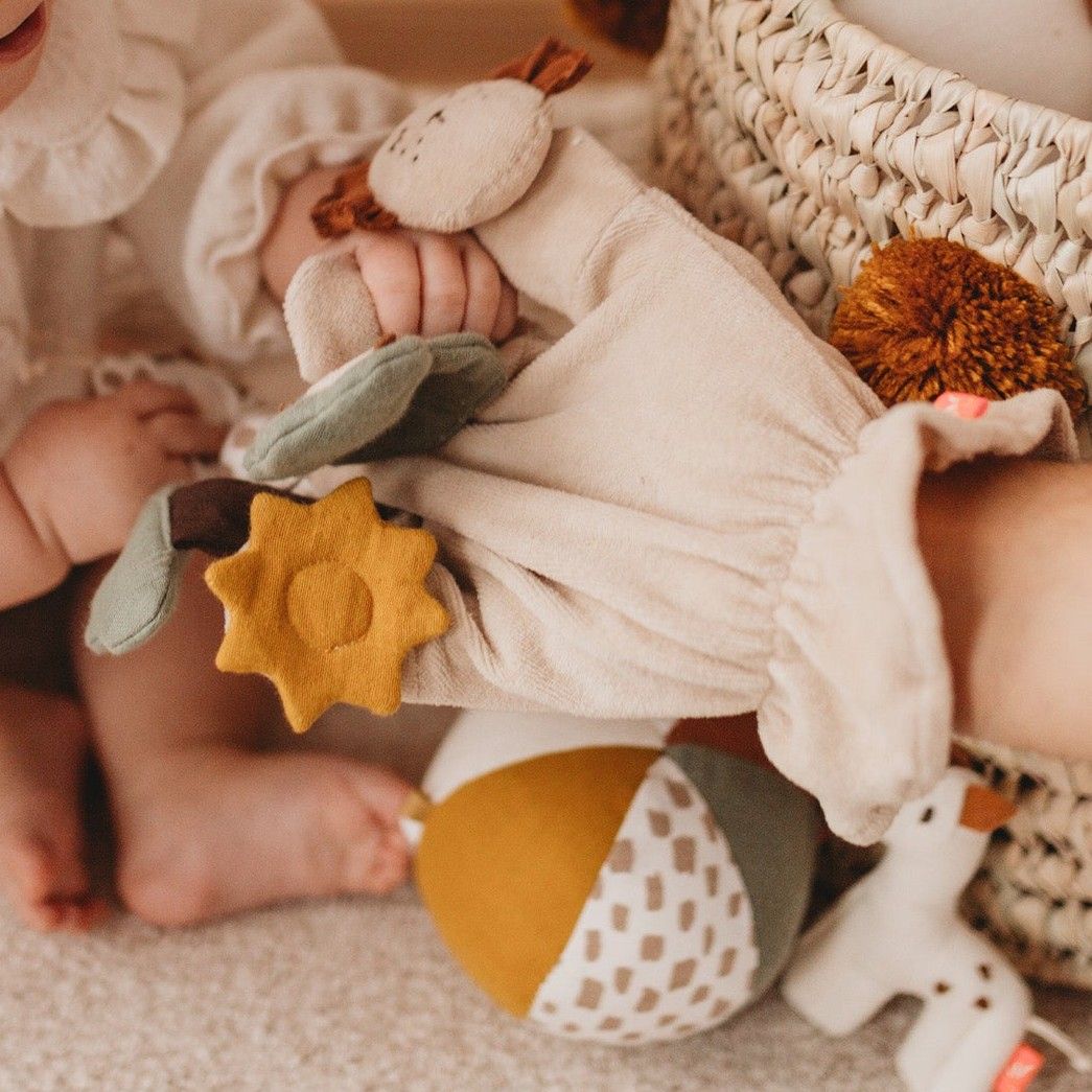 Babyhände greifen nach Fingerspielfigur Giraffe. Beige Stoffhandschuh mit Giraffen-, Löwen- und Blattformen. Gelber Stern.