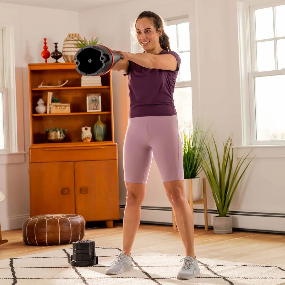 Personne s'entraînant avec une kettlebell. Haltère kettlebell noire avec bande rouge. Marque Bowflex.