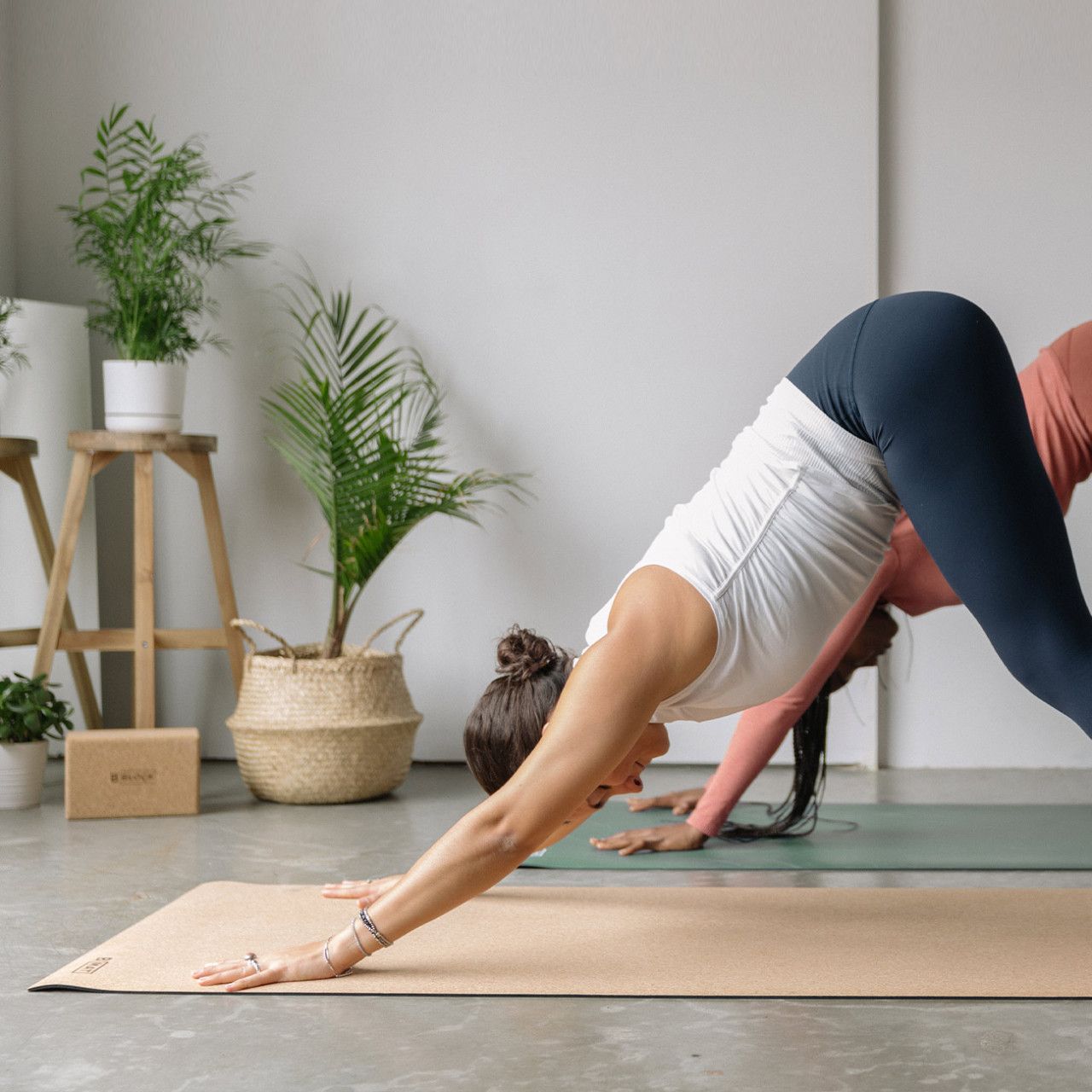 Zwei Frauen praktizieren Yoga auf Yogamatten. Eine Matte ist aus Naturkork, die andere grün.