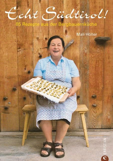 Buchcover: Echt Südtirol! 85 Rezepte. Frau mit Schürze hält Tablett mit Gebäck. Holz Hintergrund.