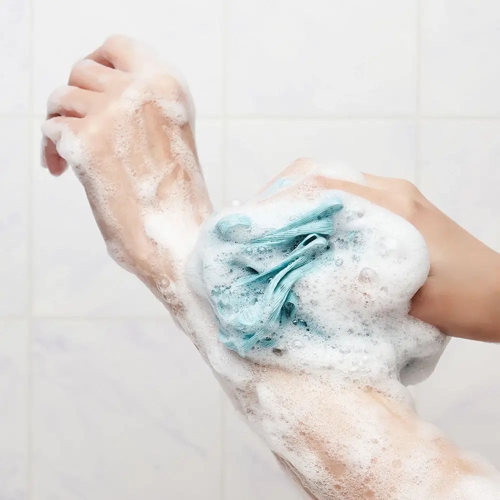 Hände mit Schaum und blauem Schwamm. Hintergrund: Kacheln. Schaumtextur.