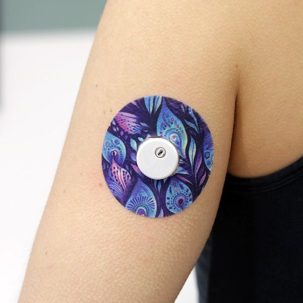 Arm mit rundem Pflaster. Pfauenfeder-Muster. Weißer Sensor in der Mitte.