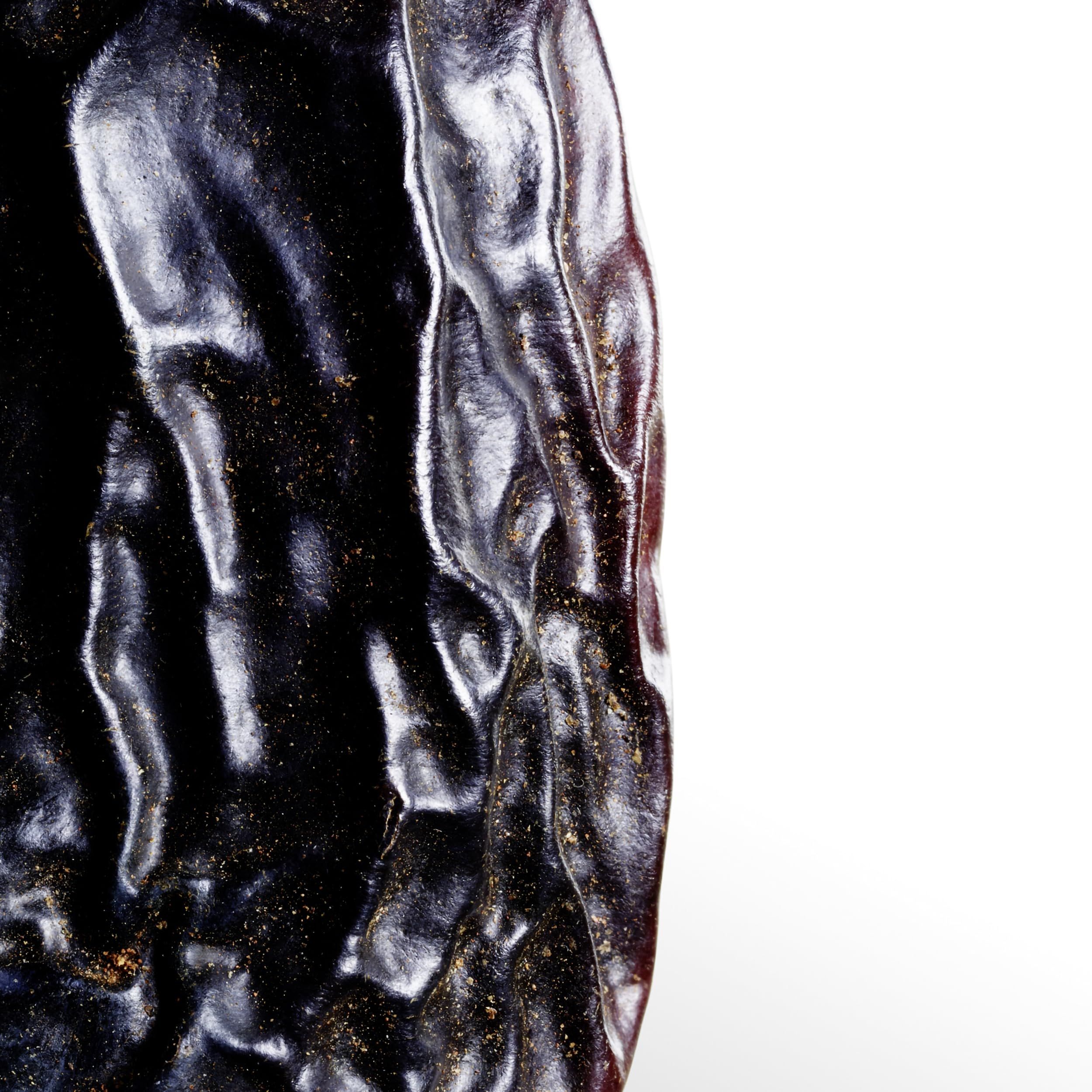 Nahaufnahme einer dunklen, strukturierten Oberfläche. Goldene Partikel sind sichtbar. Die Oberfläche ist gewellt.