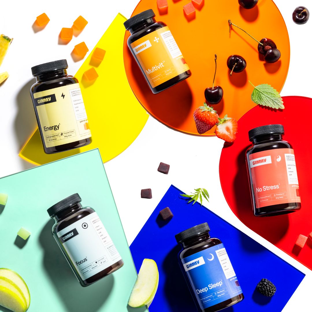 GIMMY Originals Nahrungsergänzungsmittel, fünf Flaschen und Gummibärchen. Auf farbigen Hintergründen, mit Obst.