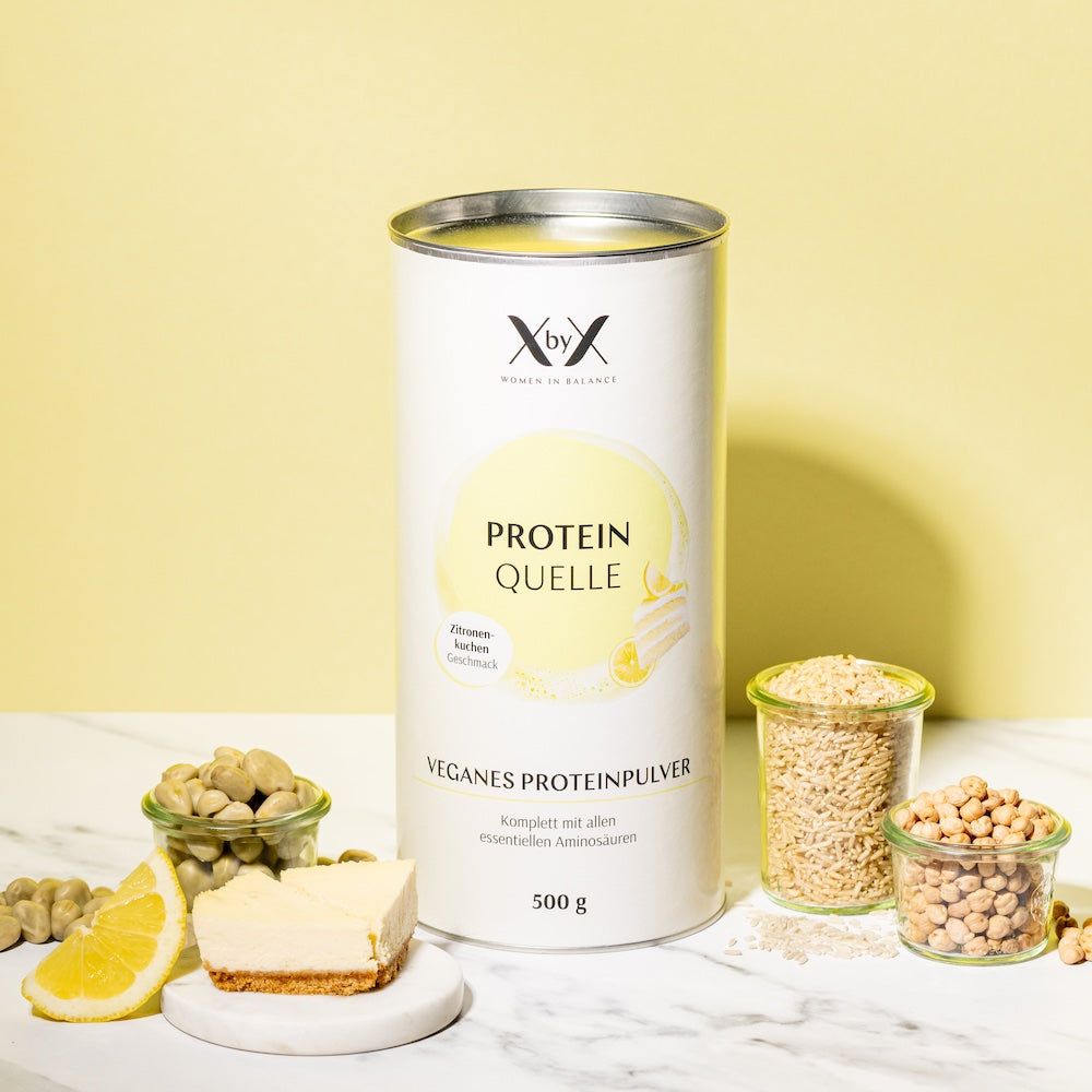 Zylindrische Dose mit XbyX-Logo und Aufschrift Protein Quelle. Veganer Proteinpulver, Zitronenkuchen-Geschmack. 500g. Dazu Zitrone und Kuchen.