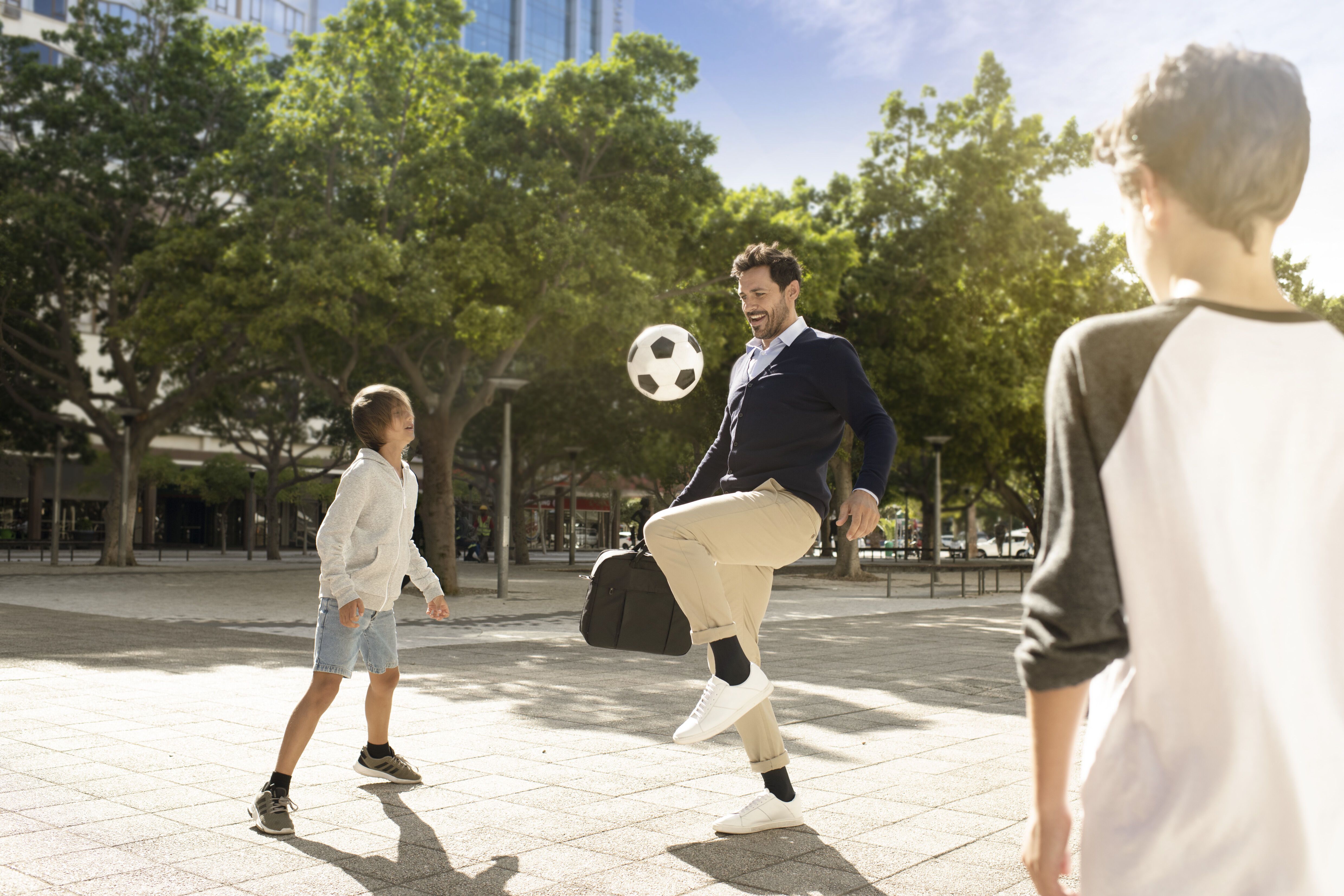 Vader en kinderen spelen voetbal. Man met zwarte compressiekousen. Achtergrond van stadspark.