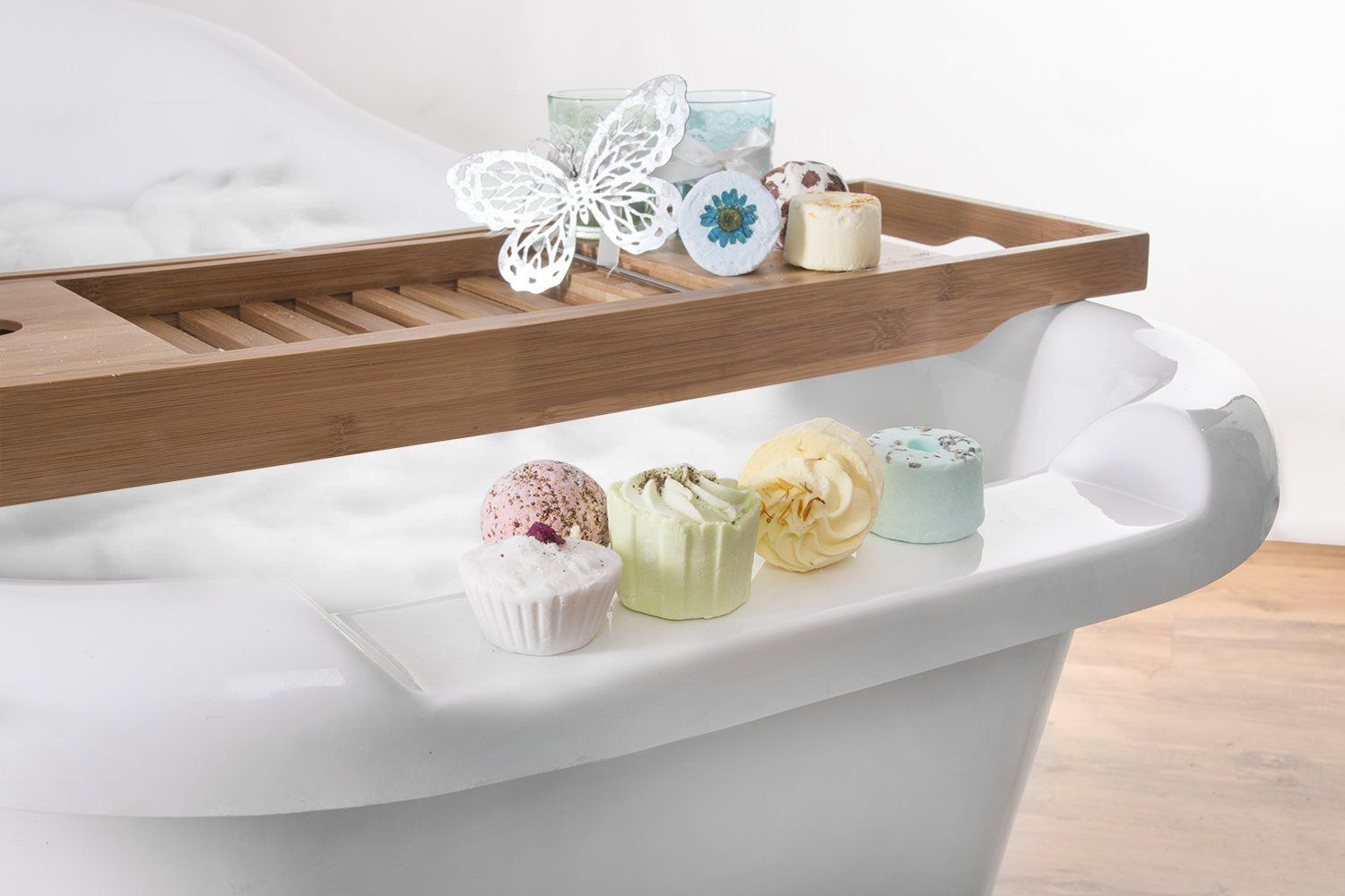 Badebomben und -kuchen auf einer weißen Oberfläche, im Hintergrund eine Badewanne. Verschiedene Formen und Farben.