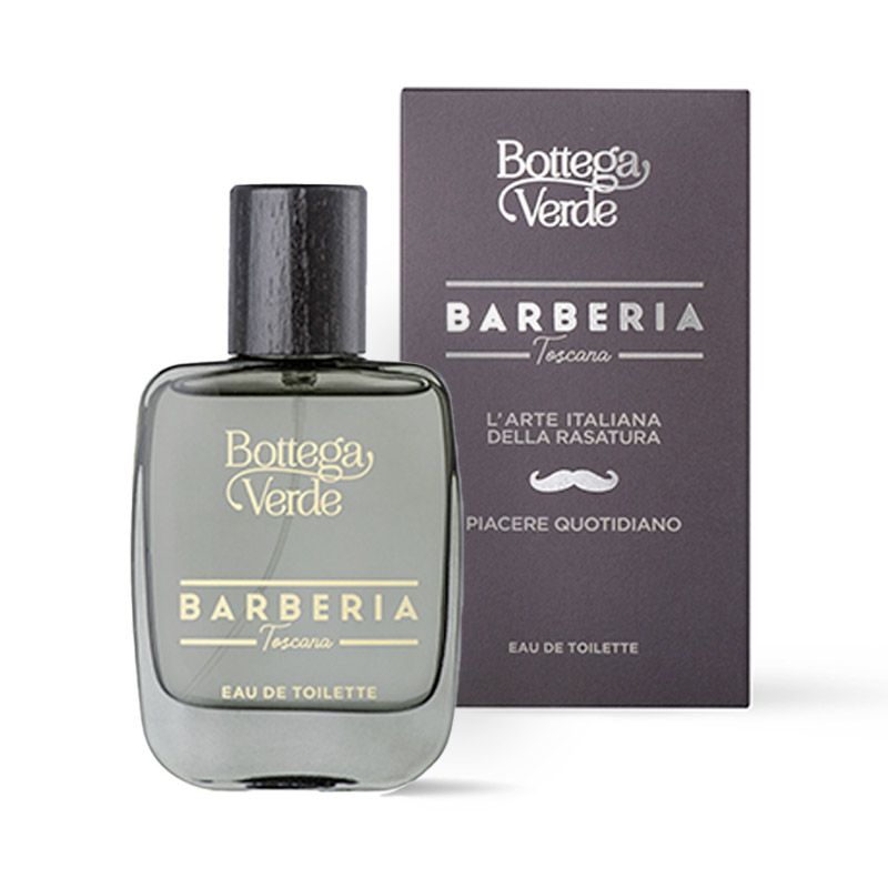 Bottega Verde Barberia Toscana eau de toilette. Una bottiglia di vetro grigio con un tappo in legno scuro è presentata accanto a una scatola grigia. Il nome del marchio e il nome del prodotto sono visibili sulla bottiglia e sulla scatola. La scatola mostra anche un paio di baffi e del testo italiano.