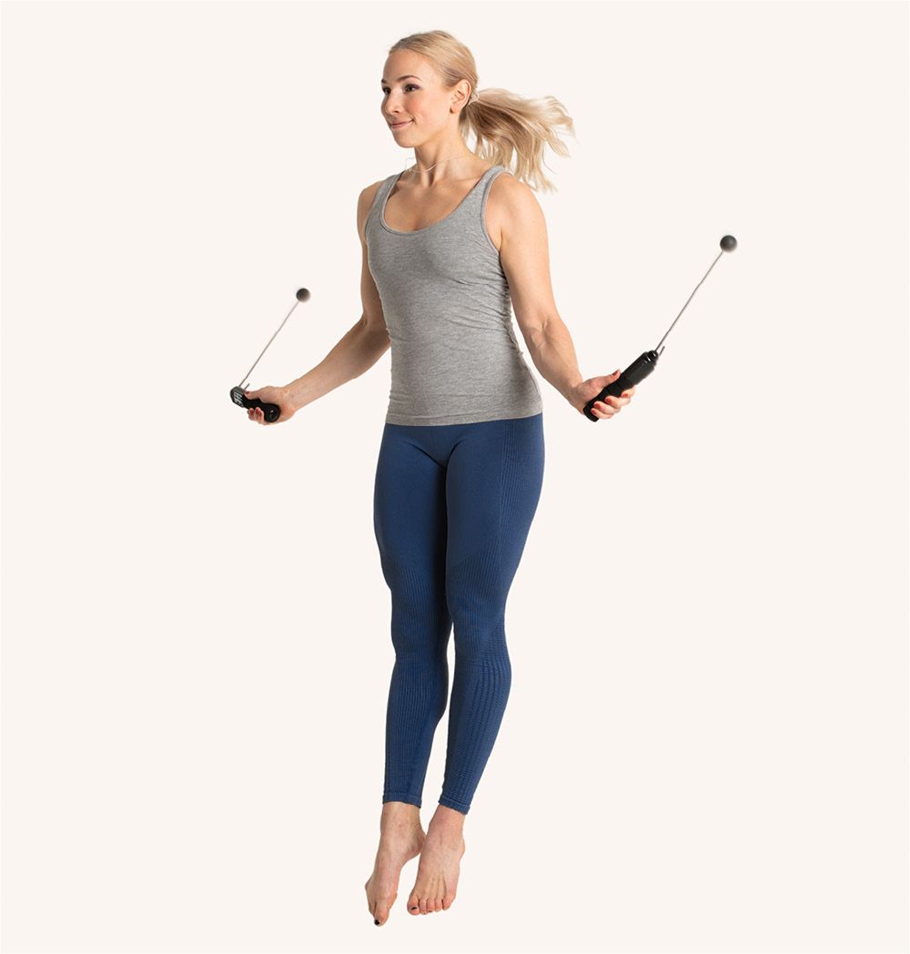 Frau springt mit digitalem Springseil. Schwarze Griffe, Kugeln an den Enden. Blaue Leggings, graues Top.