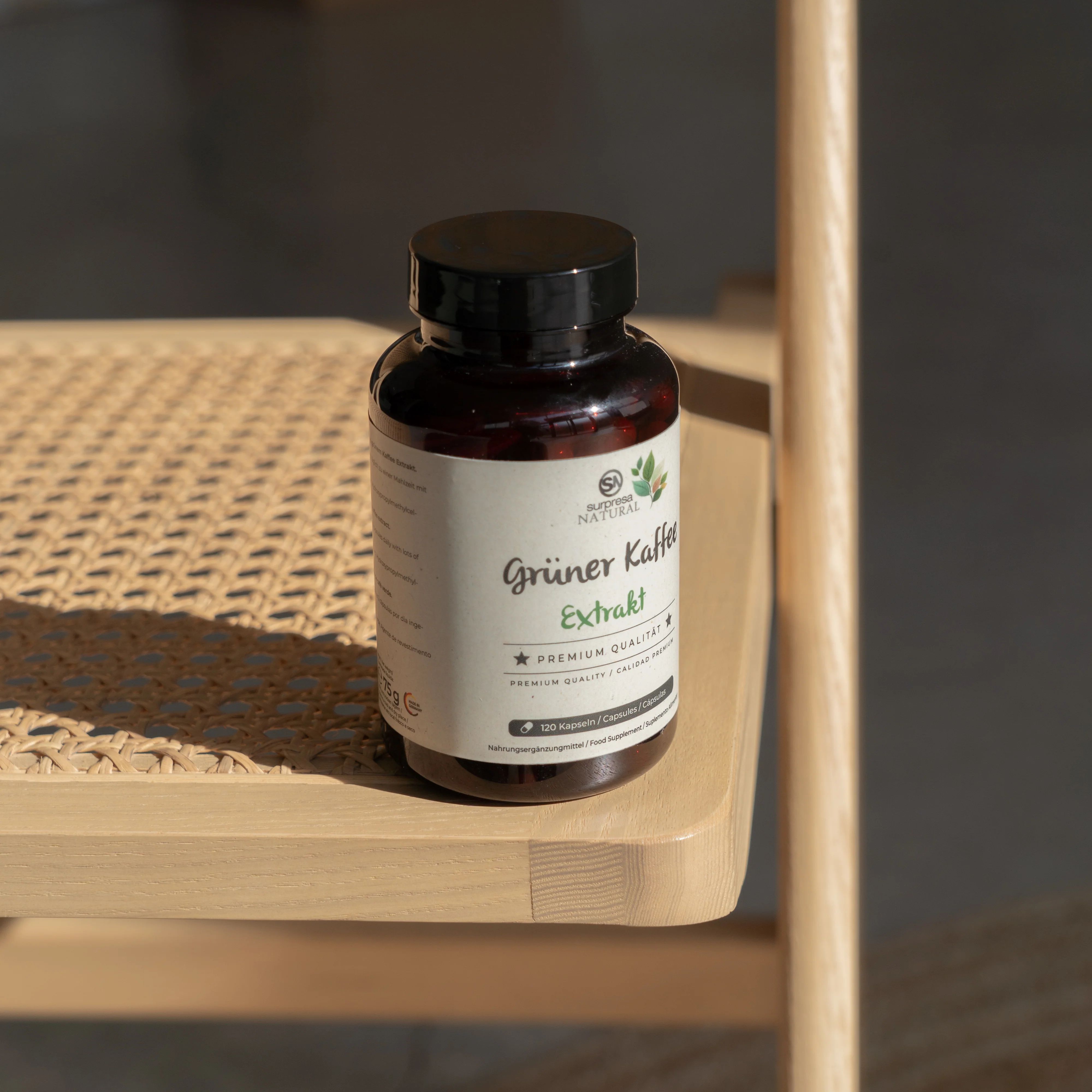 Braune Flasche mit Etikett auf einem Stuhl. Aufschrift: Grüner Kaffee Extrakt. Logo: Blätter und "Surpresa Natural".