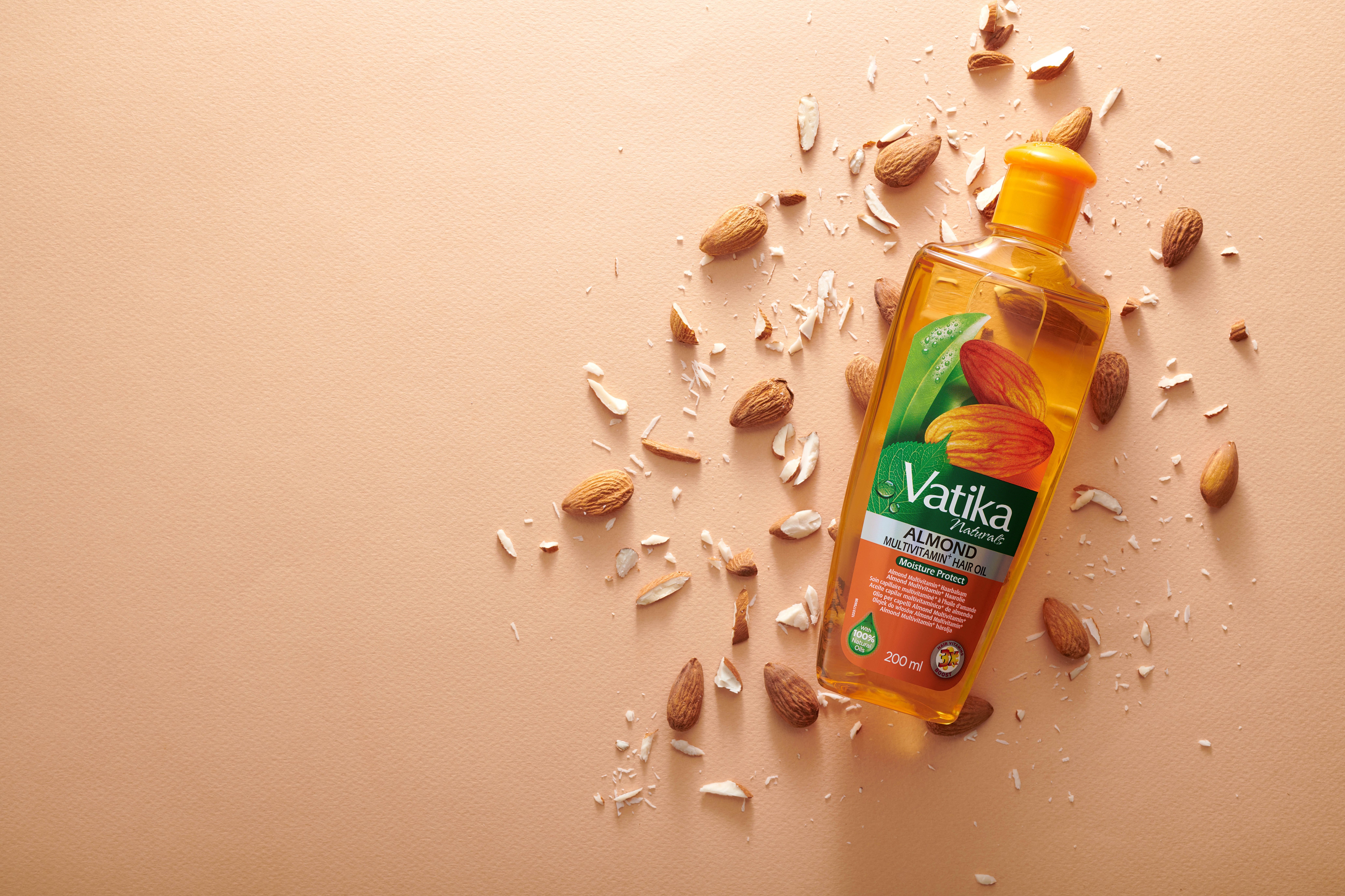 Flasche mit Haaröl, umgeben von Mandeln und Mandelstücken. Aufschrift: Vatika Almond Multivitamin Hair Oil.