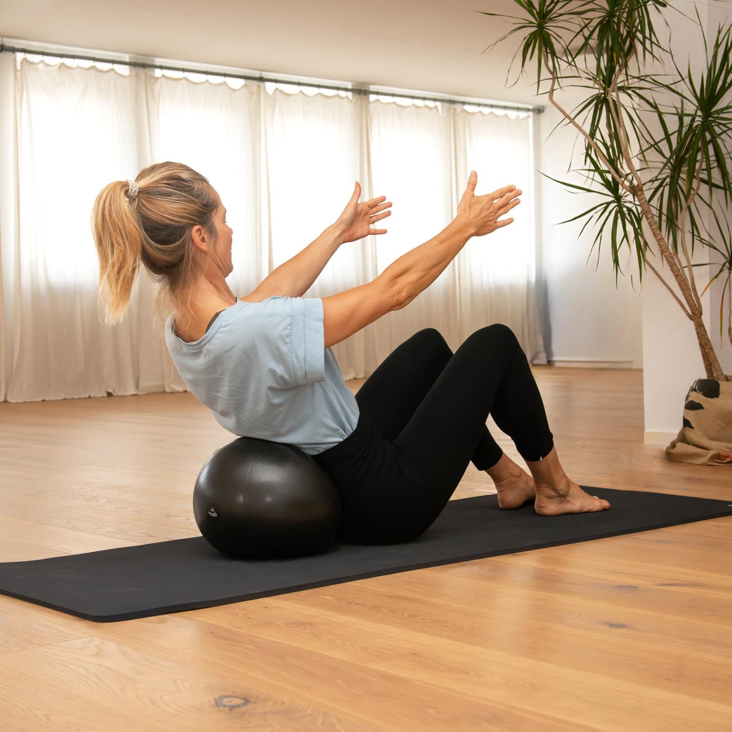 Frau macht Pilatesübungen mit einem anthrazitfarbenen Ball auf einer Matte.
