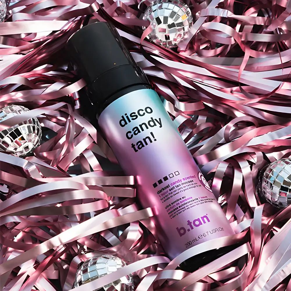 Selbstbräunungsmousse-Flasche mit schwarzem Sprühkopf. Aufschrift: disco candy tan! und b.tan. Auf rosa Konfetti und Spiegelkugeln.