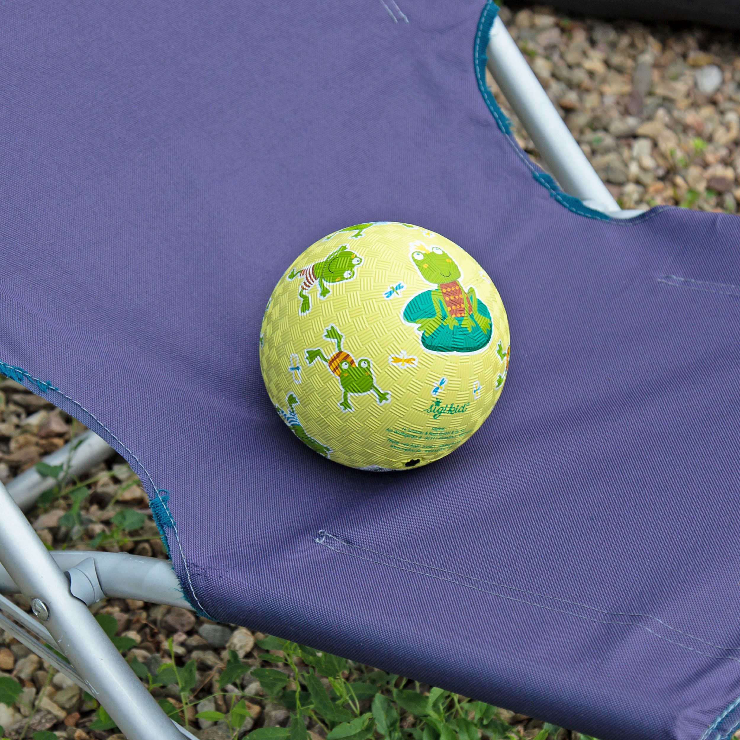 Gelber Ball mit Frosch-Motiven auf einem lila Stuhl. Ball liegt auf dem Stuhl.