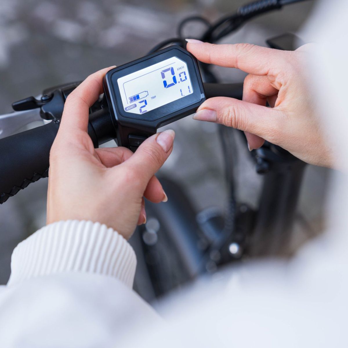 Hände halten ein Display. Schwarzer Rahmen, weißer Bildschirm mit Ziffern. Anzeige von Geschwindigkeit und Akku.