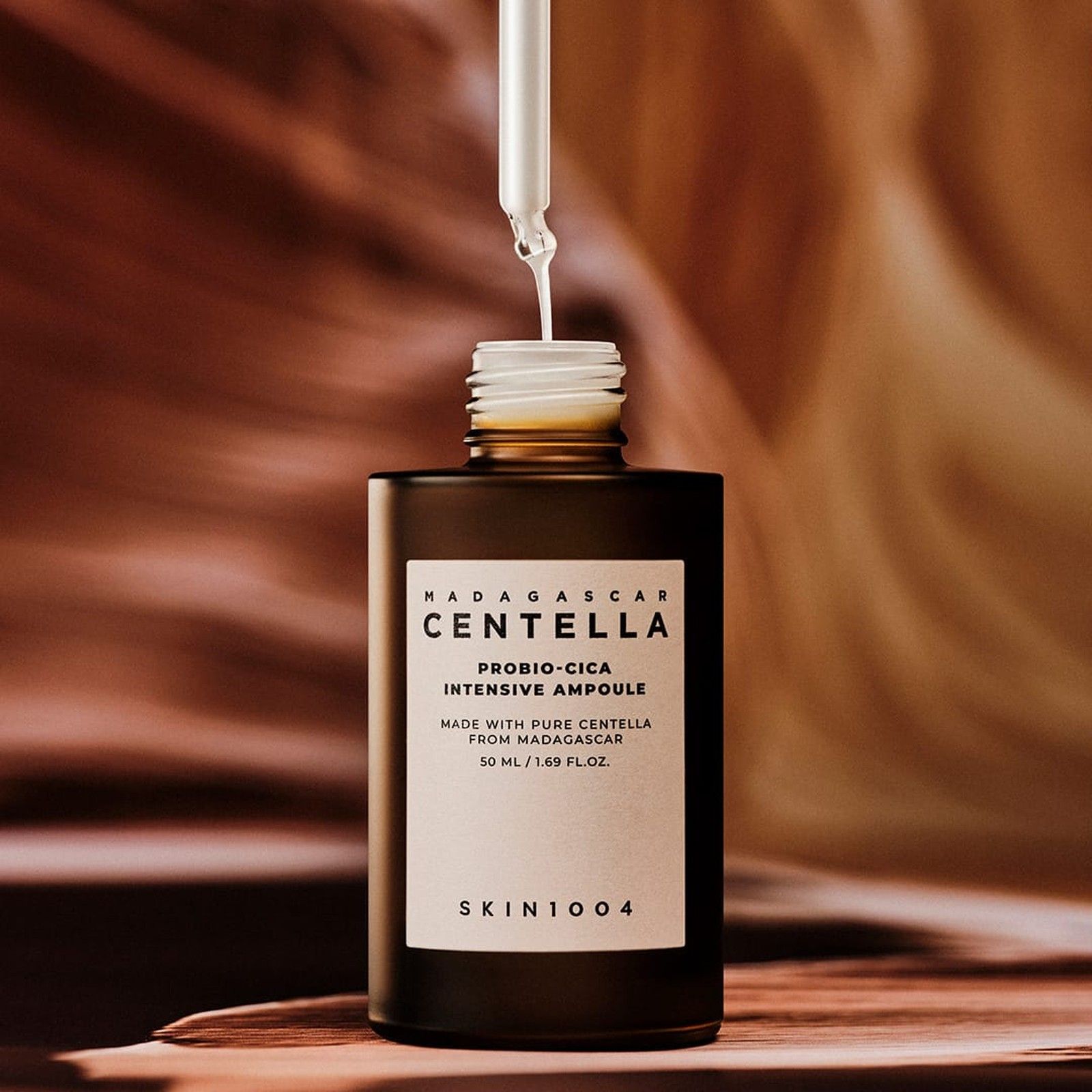 Pipette tropft Serum in eine offene braune Flasche, Etikett 'Centella Probio-Cica Intensive Ampoule'.