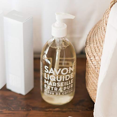 Transparente Flasche mit weißem Pumpkopf, neben einer Box und einem Korb. Aufschrift: Savon Liquide Marseille Extra Pur Fleur de Coton.