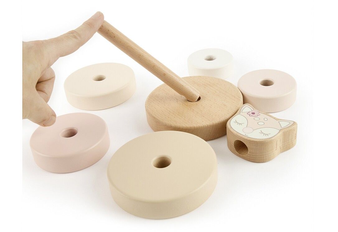 Stapelturm-Teile: Holzsockel, Ringe, Reh-Kopf. Einzelteile liegen. Hand zeigt auf Holzstab. Pastelltöne.