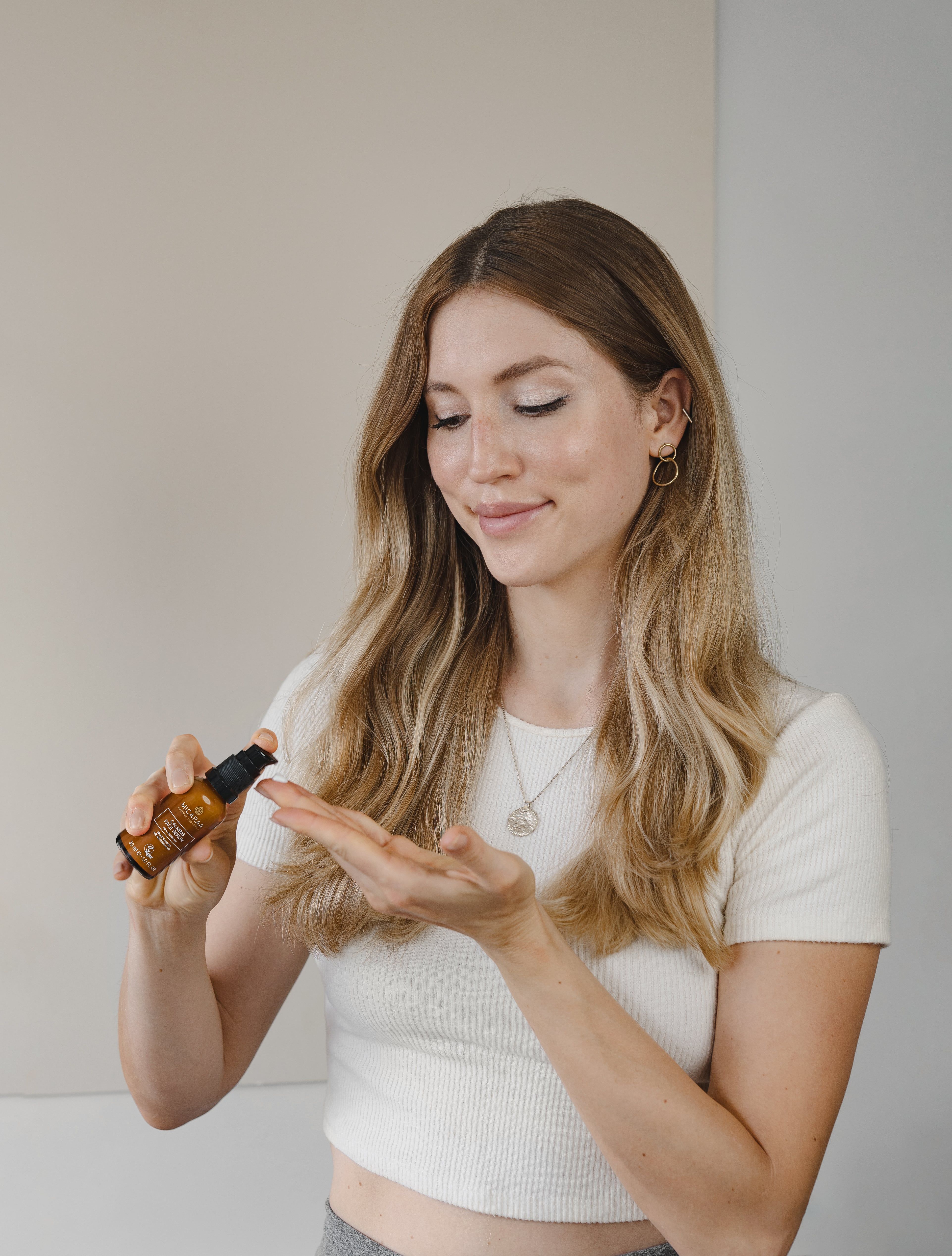Frau hält eine braune Flasche mit schwarzem Pumpkopf. Aufschrift: MICARAA Calming Face Serum. Vegan-Siegel. 30 ml.