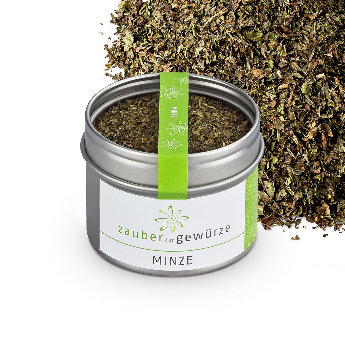Metallbehälter mit getrockneter Minze. Etikett mit "Zauber der Gewürze Minze". Grünes Band mit "Minze". Getrocknete Minze daneben.