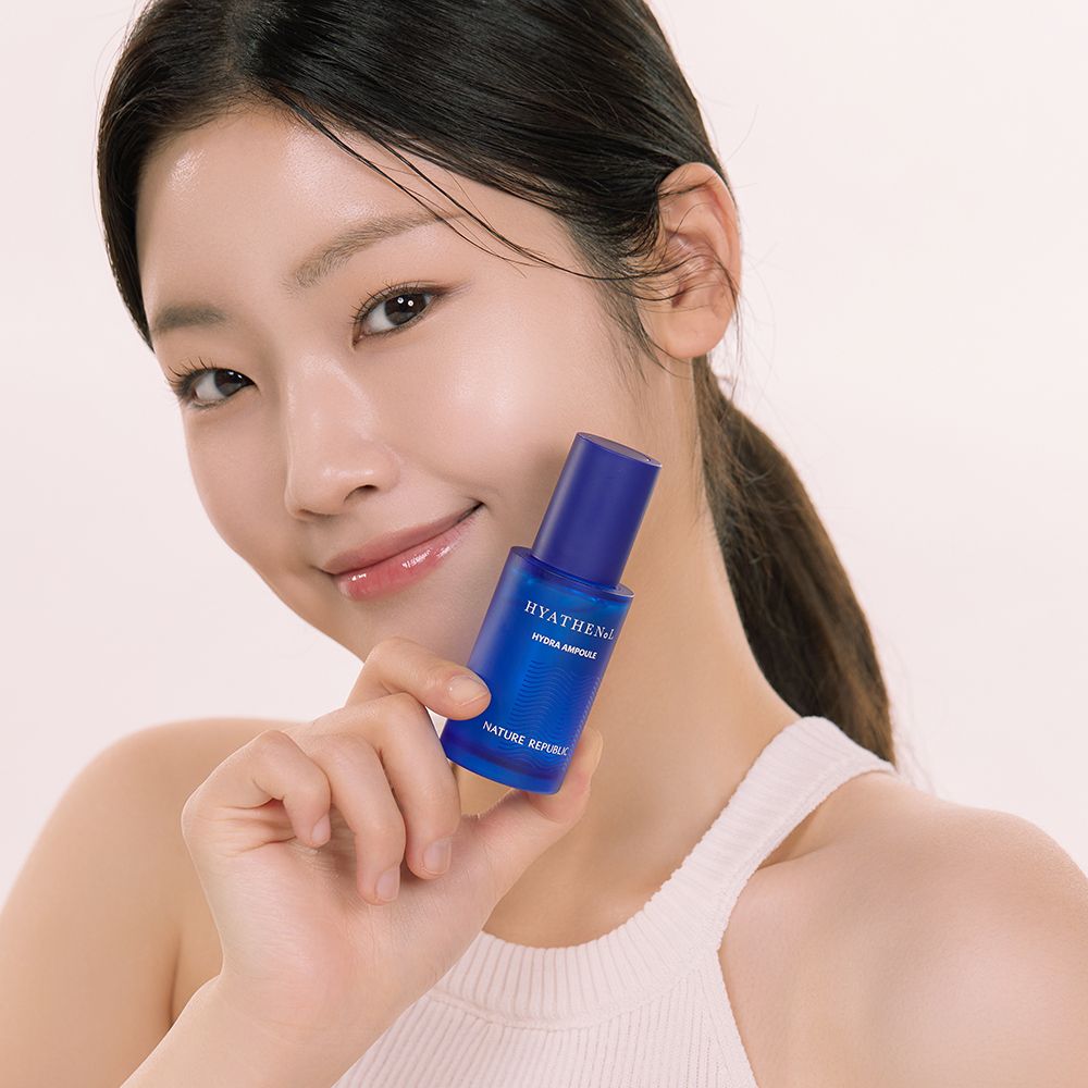 Frau hält blaue Serumflasche. Schriftzug HYATHENOL, Hydra Ampoule und NATURE REPUBLIC. Frau lächelt.