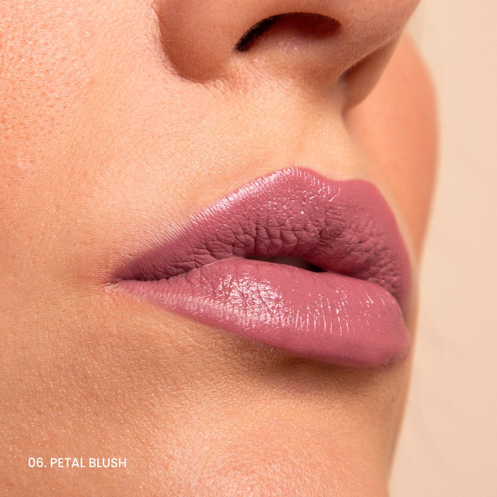 Primo piano di labbra truccate con rossetto rosa. Sotto le labbra c'è scritto "06. PETAL BLUSH".