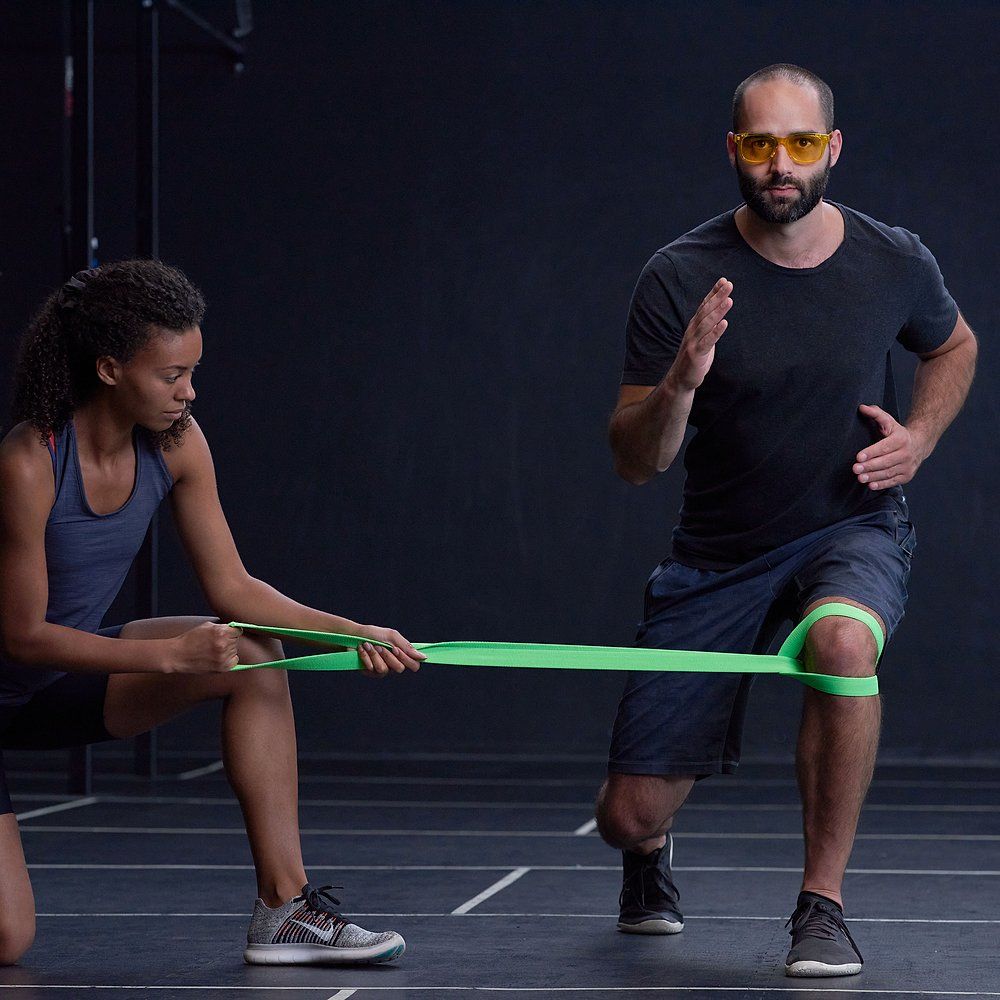 Zwei Personen im Fitnessstudio. Eine Person mit orangefarbener Brille. Widerstandsband.