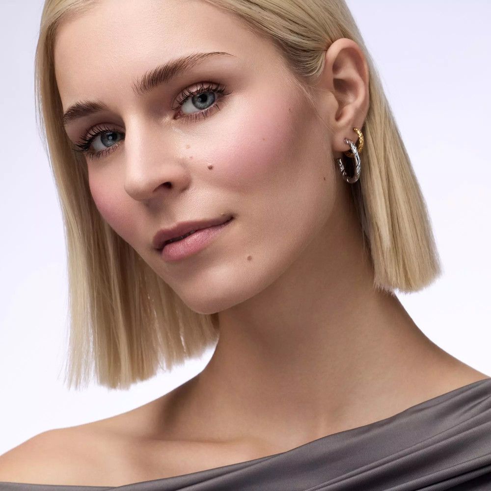 Nahaufnahme einer Frau mit blonden Haaren und Ohrringen. Ihr Blick ist nach oben gerichtet.