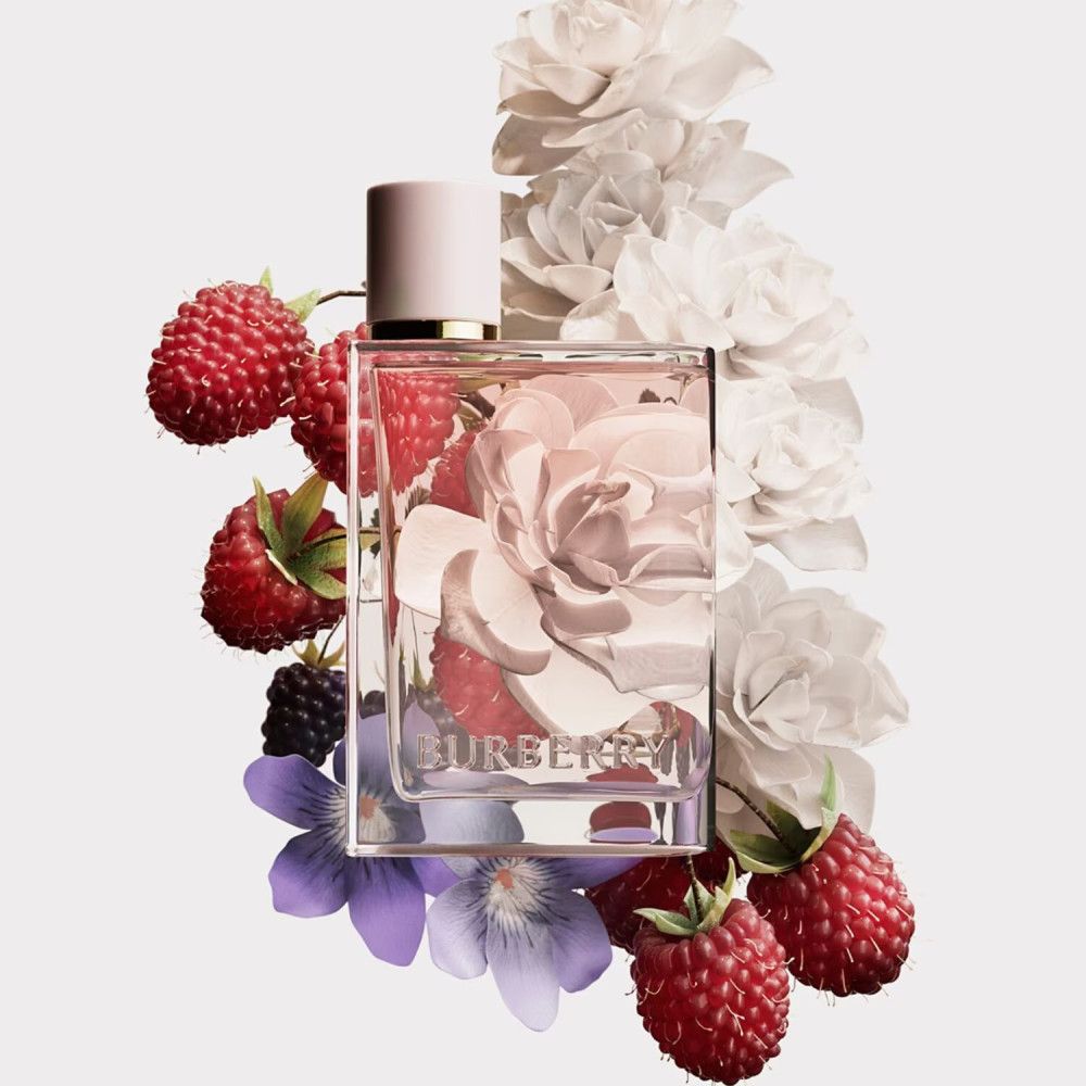 Burberry Her Eau de Parfum-Flakon, umgeben von Himbeeren, Brombeeren, Blüten und Blumen. Der Flakon ist quadratisch.