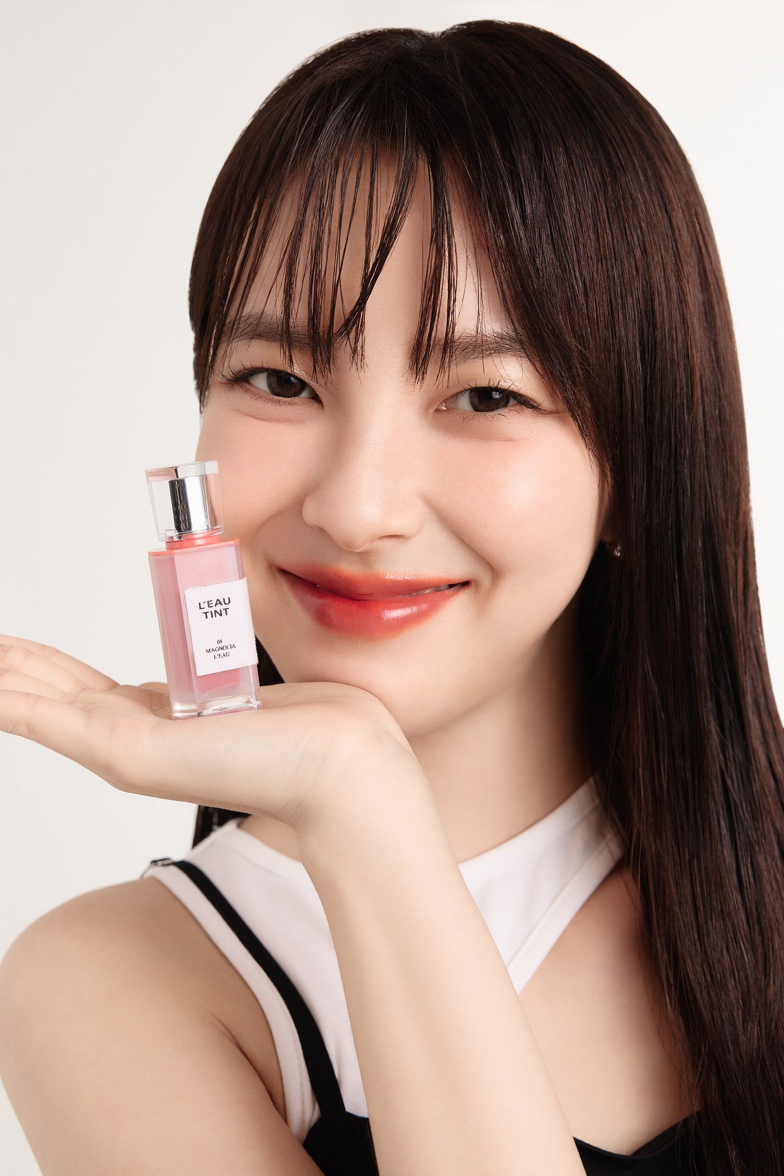 Frau hält eine kleine Flasche Lippenfarbe. Sie lächelt. Helle Haut, dunkle Haare.