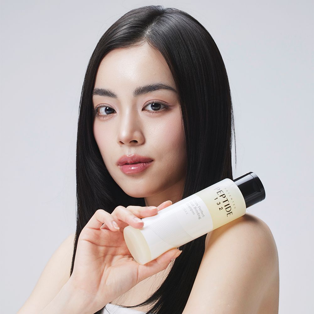 Frau mit langen dunklen Haaren hält eine Flasche PEPTIDE-132 Shampoo.