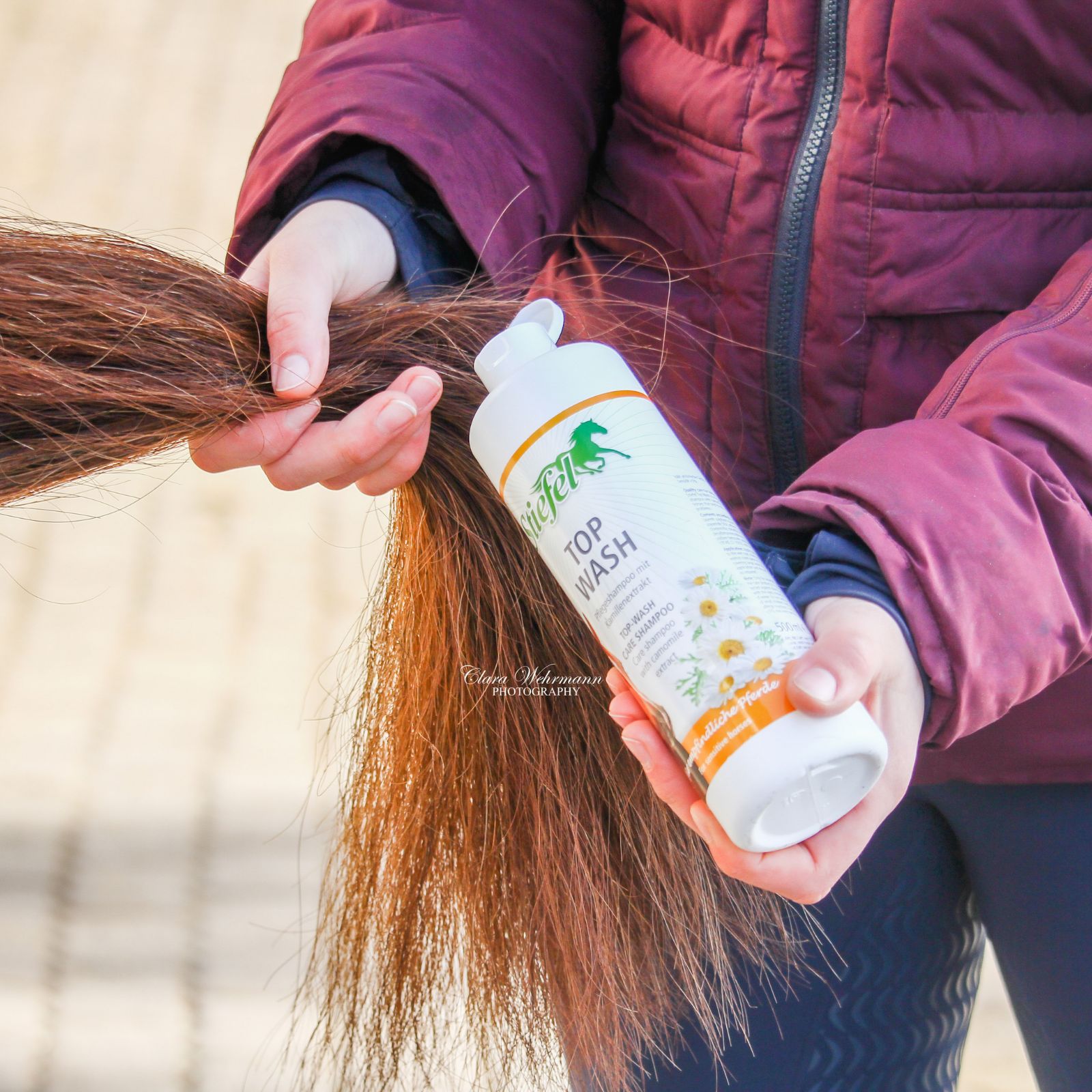 Person hält eine Flasche Stiefel Top Wash Shampoo. Produktetikett mit Kamillenblüten und Pferdeabbildung.