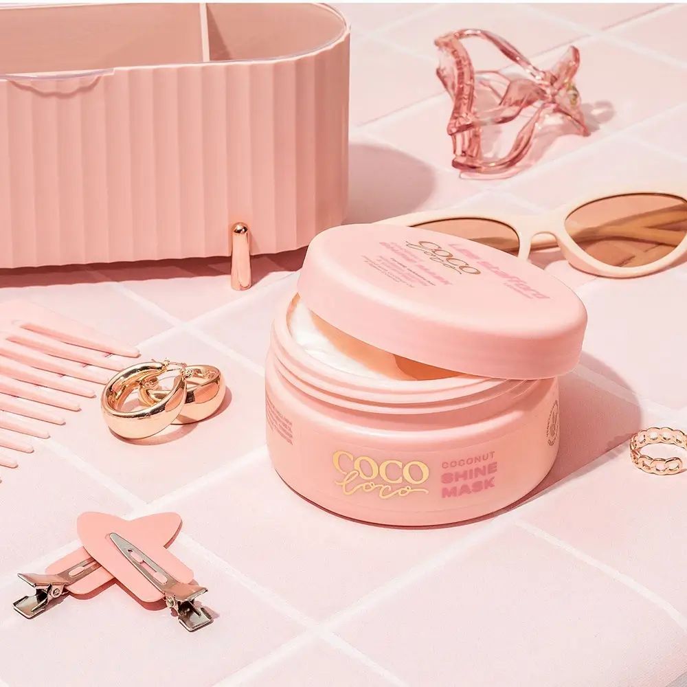 Geöffnete, rosa Dose Coco Loco, Coconut Shine Mask. Daneben Accessoires: Haarklammern, Sonnenbrille, Schmuck.
