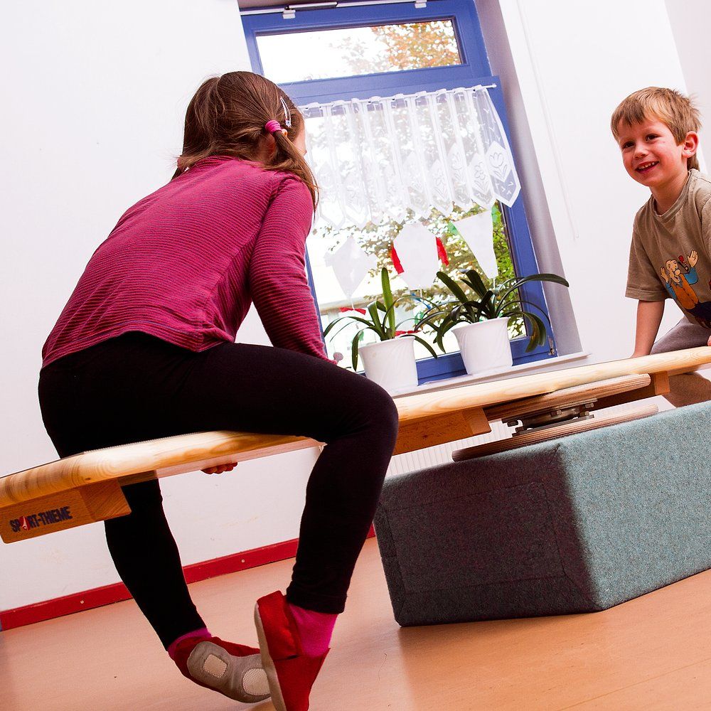 Kinder auf einem Karussell-Element. Holzkonstruktion mit Drehscheibe und Sitzfläche. Zwei Kinder interagieren.