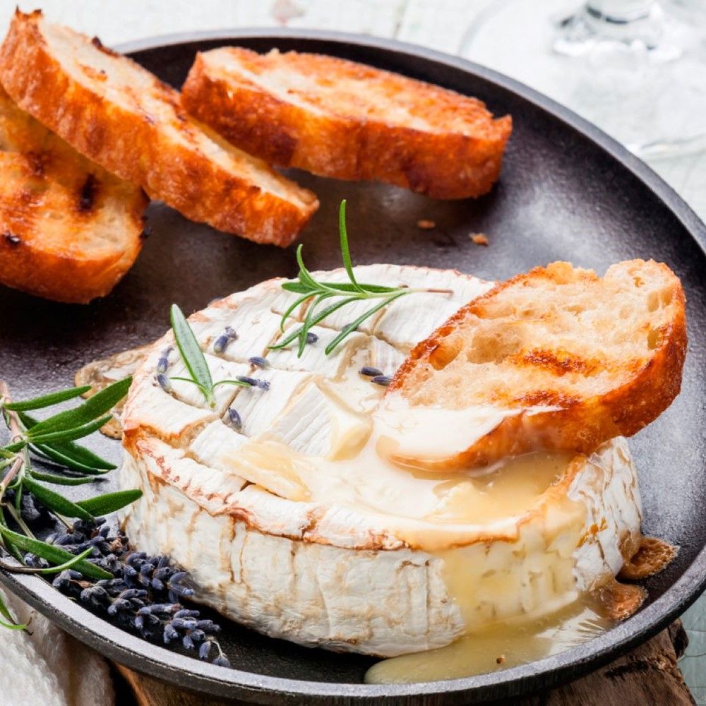 Runder Käse auf schwarzer Platte mit Brot, Rosmarin und Lavendel.