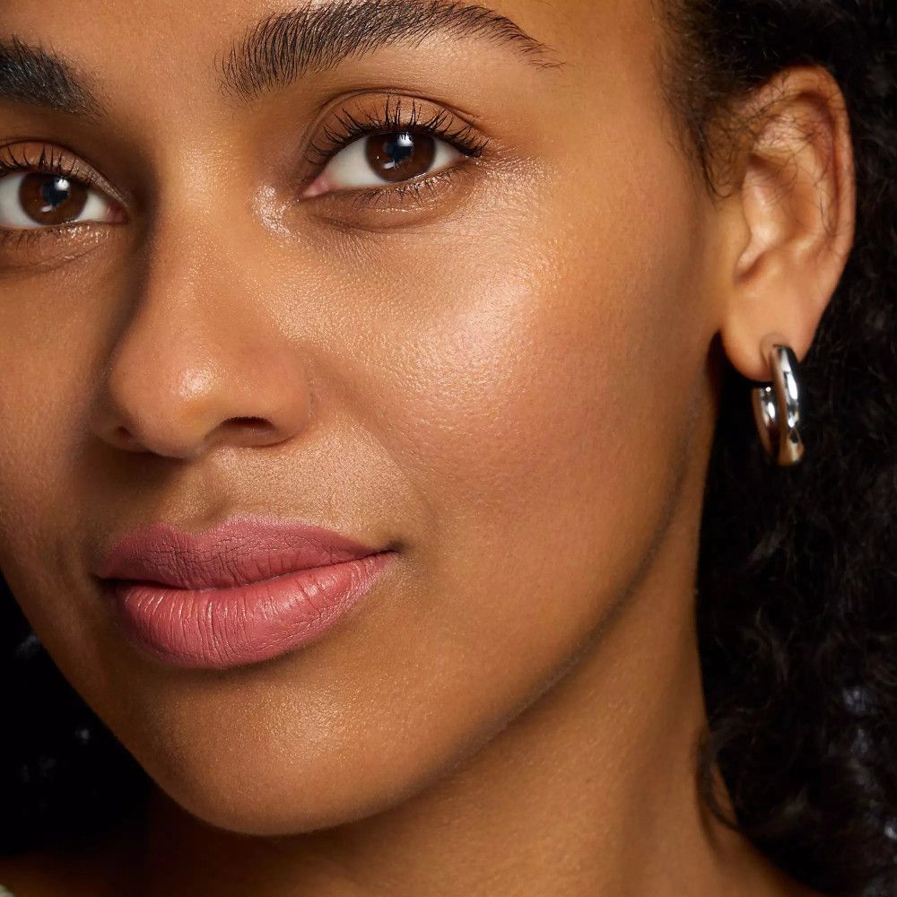 Nahaufnahme eines Gesichts mit Lippen, die mit Catrice Creamy Nudes Lippenkonturenstift geschminkt sind. Frau mit silbernen Ohrringen.