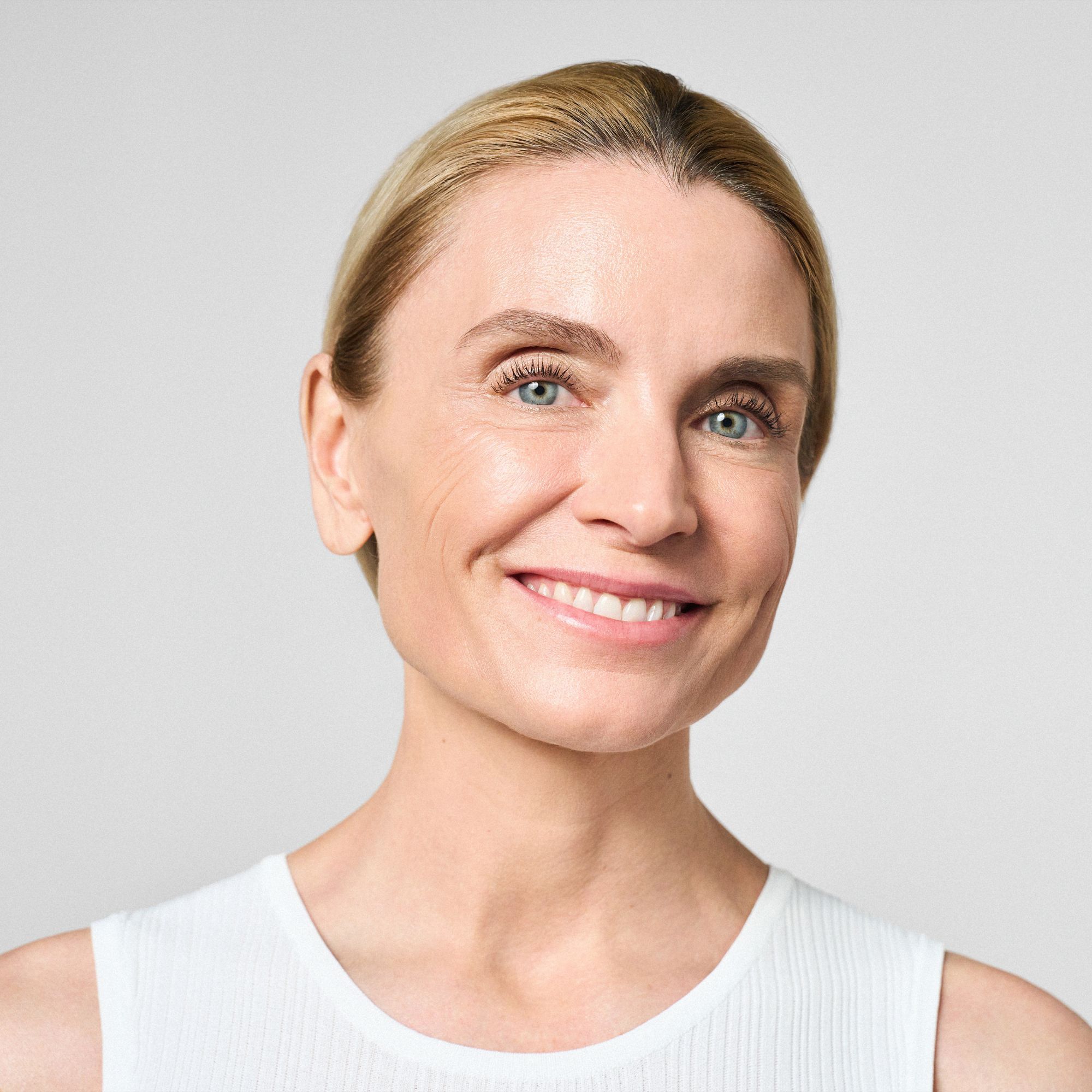 Porträt einer Frau mit blonden Haaren und weißem Top. Sie lächelt in die Kamera.