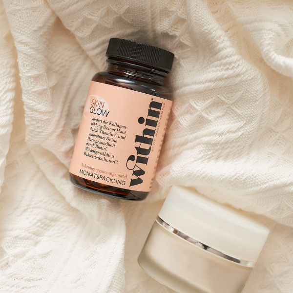Braune Flasche Skin Glow und Creme-Tiegel auf weißem Stoff. Beide Produkte sind auf dem Etikett beschriftet.