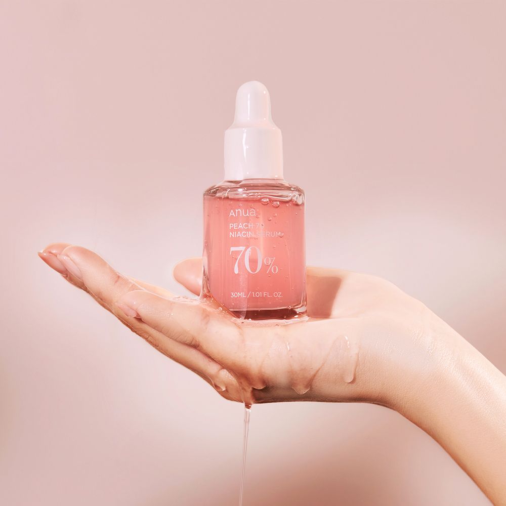 Hand hält Anua Peach 70 Niacin Serumflasche, Serum tropft.