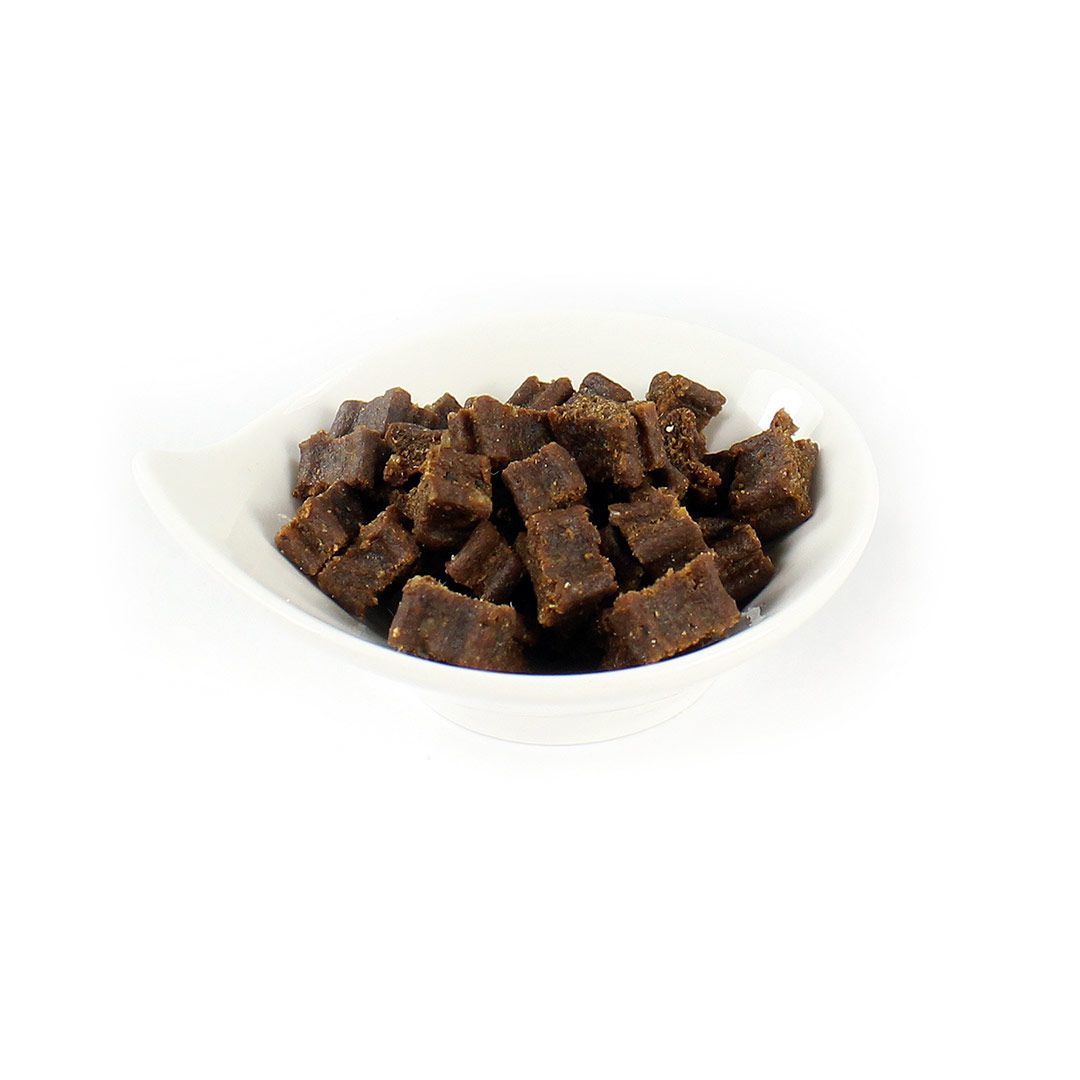 Braune, würfelförmige Snacks in einer weißen, geschwungenen Schale. Nahaufnahme, vor weißem Hintergrund.