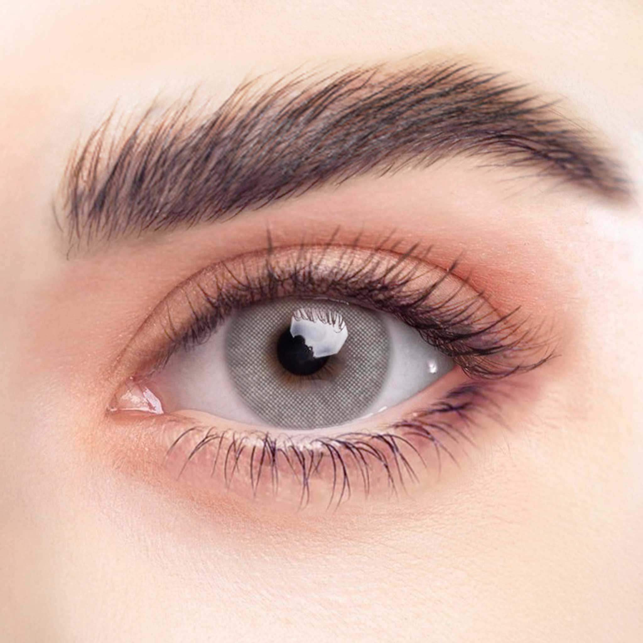 Nahaufnahme eines Auges mit grauer Kontaktlinse. Sichtbare Wimpern und Augenbrauen. Die Linse hat ein feines, strukturiertes Muster.