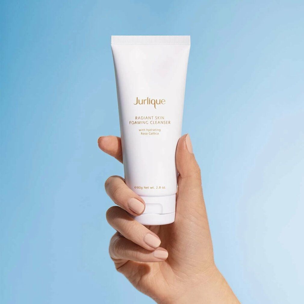 Hand hält Jurlique Radiant Skin Foaming Cleanser Tube vor blauem Hintergrund.