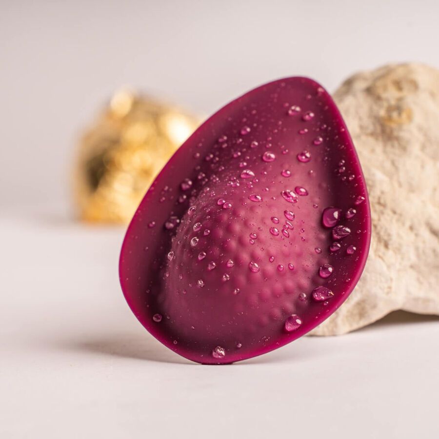 Dunkelrotes, ei-förmiges Produkt mit Wassertropfen. Oberseite mit erhabenen Punkten.