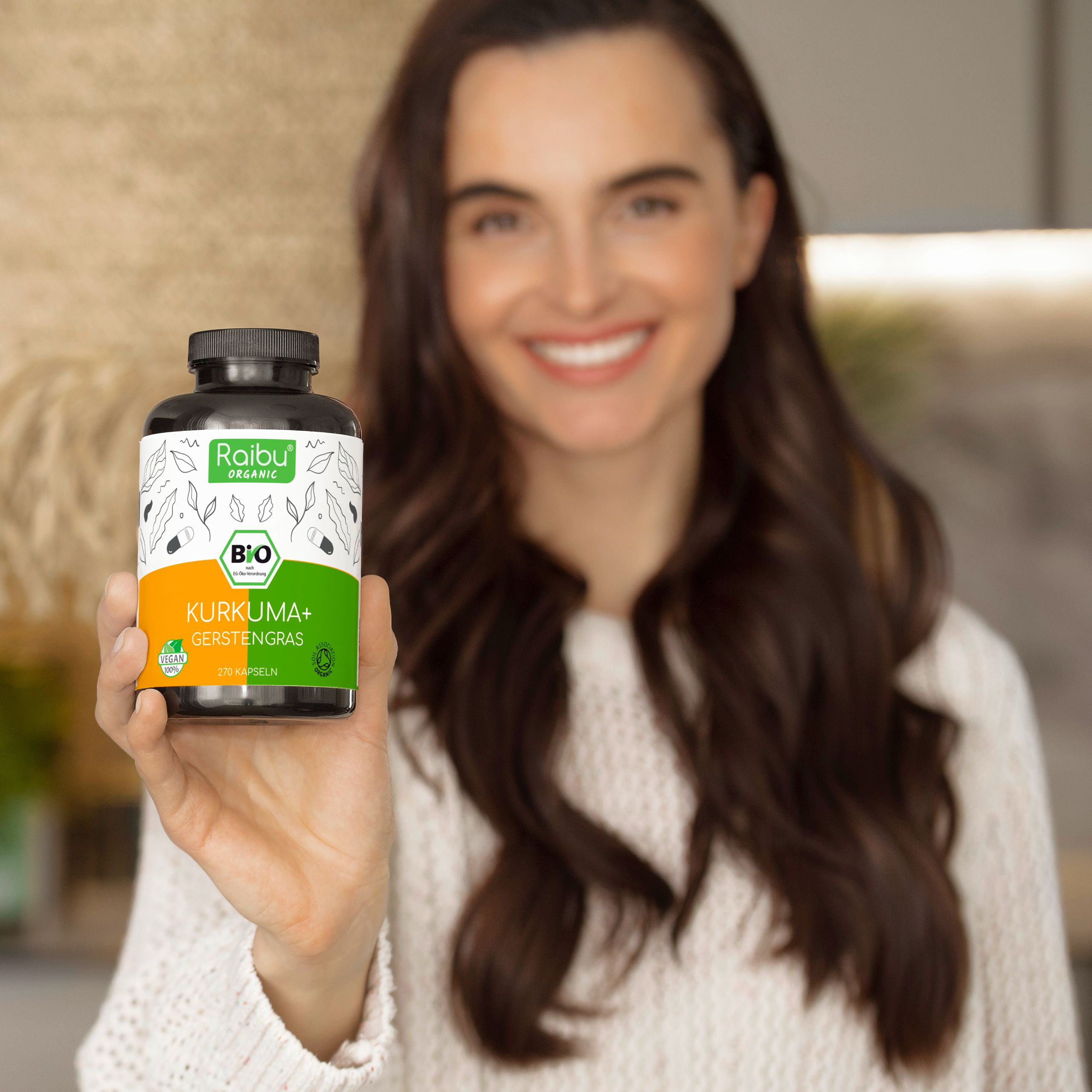 Frau hält Flasche. Aufschrift: Raibu Organic, Kurkuma+ Gerstengras, Bio-Siegel.